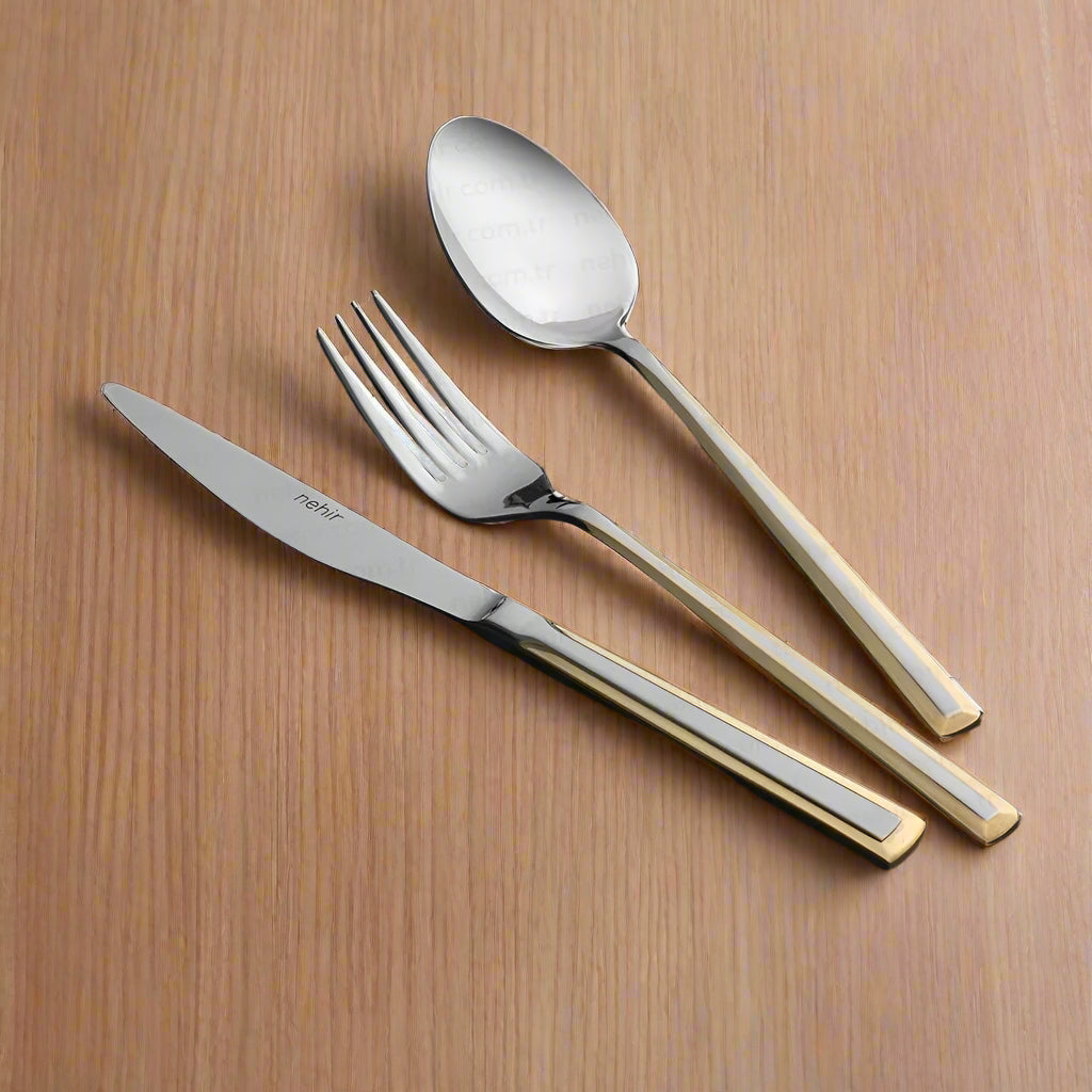 A selection of cutlery with golden handles on a black plate, including a spoon, fork, and knife.