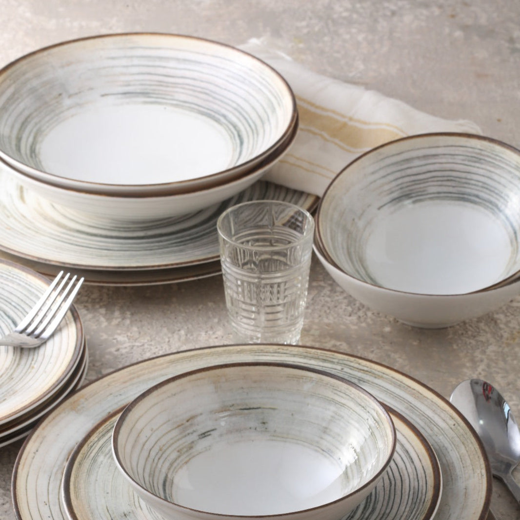 A porcelain dinner set with beige and brown striped patterns around the rim of the plates and bowls, displayed on a table with some cutlery visible.