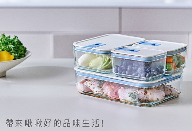 A person holding a square-shaped food storage container with a blue silicone lid, in a refrigerator filled with various other containers.